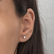 Close-up of an ear wearing a diamond stud earring with a blurred background