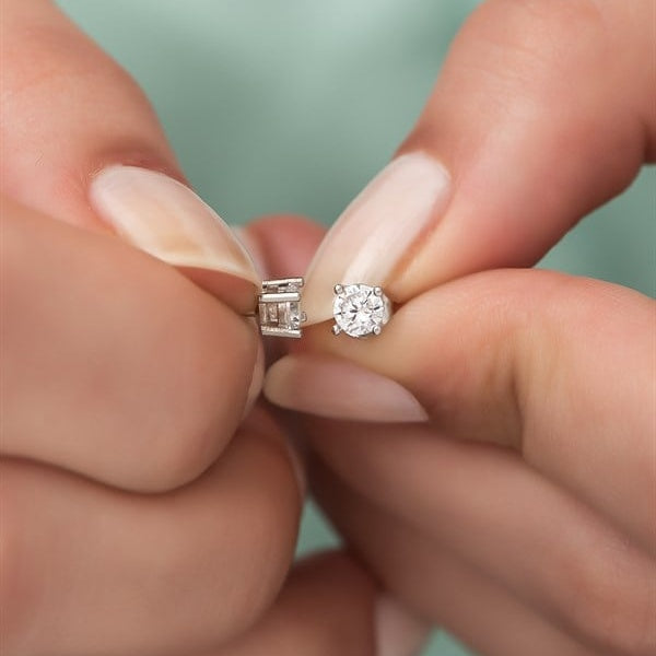 Two diamond earrings held between fingers against a blurred background