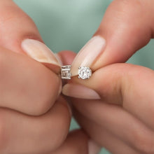 Two diamond earrings held between fingers against a blurred background