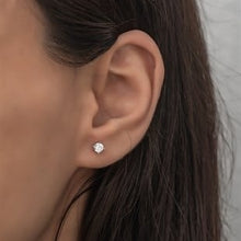Close-up of an ear wearing a diamond stud earring with dark hair and neutral background