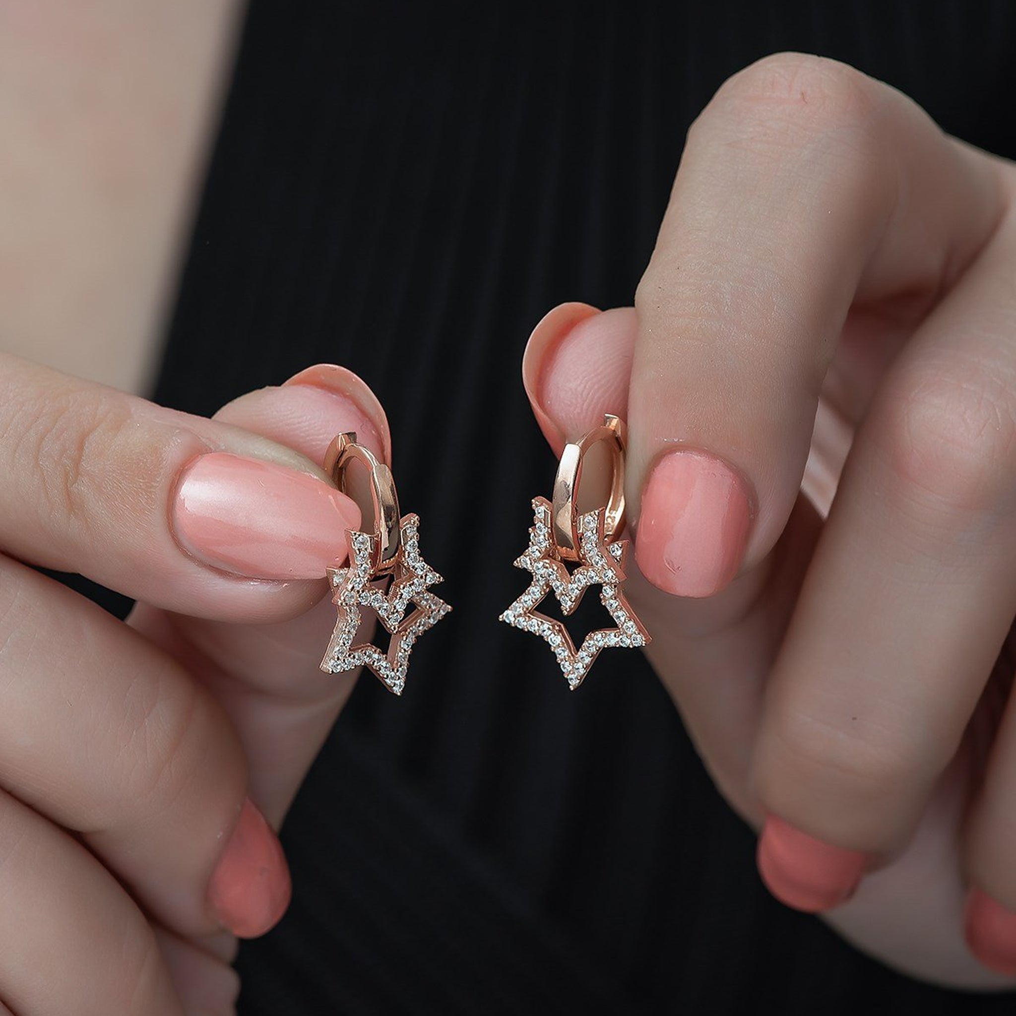 Rose gold star-shaped earrings held between fingers against a neutral background