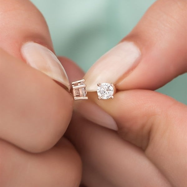 Rose gold and silver earrings held between fingers against a blurred background
