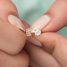 Rose gold and silver earrings held between fingers against a blurred background