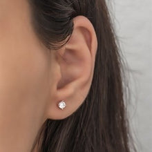 Close-up of an ear wearing a diamond stud earring with a neutral background