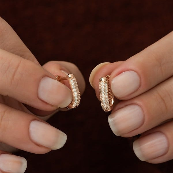 Rose gold hoop earrings held between two hands against a dark background