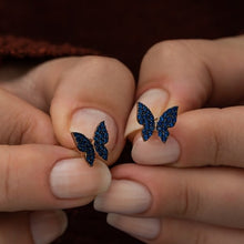 Butterfly earrings with blue gemstones held between fingers against a blurred background