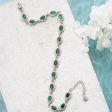 Silver bracelet with green gemstones on a white surface with flowers