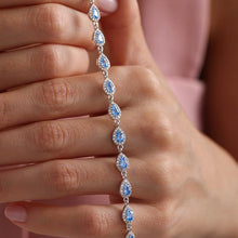 Close-up of a hand holding a silver bracelet with blue stones against a pink fabric background
