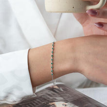 Person wearing a bracelet with green beads, holding a mug.