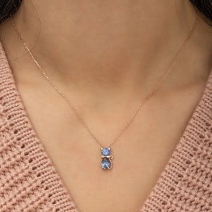 Necklace with a blue gemstone pendant worn by a person in a pink knitted cardigan.
