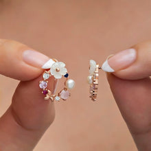Hand holding a pair of floral earrings with a soft pink background
