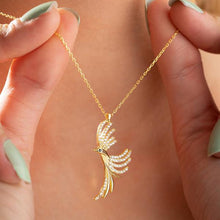 Gold necklace with a detailed pendant held by a hand against a neutral background