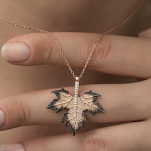 A sterling silver maple leaf necklace with rose gold plating, held between fingers.